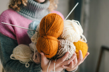 Close-up view of woman's hands holding ball of colored threads in her hands. Yarn and knitting needles.