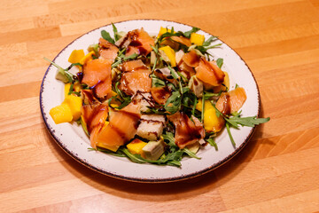 Fresh healthy salad with mango, avocado, salmon, arugula and croutons on wooden table