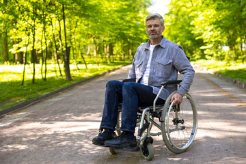Gray haired disable man in wheelchair spending free time in park.