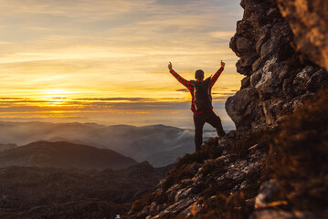 man on his back with a backpack contemplates the landscape at sunset raising his arms in victory after completing the hiking route. Sport and outdoor adventure.