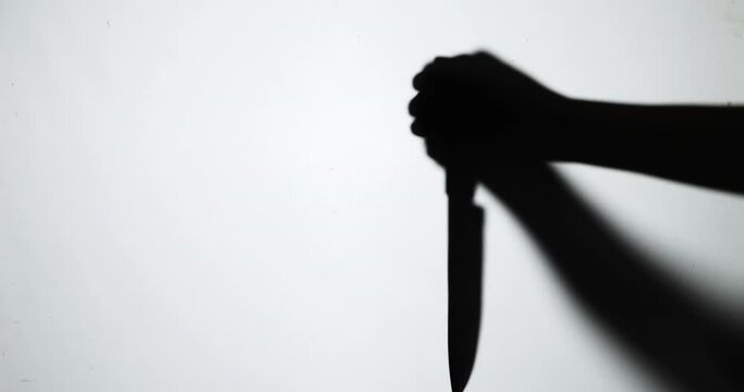 The shadow of a murderer kills his victim with a knife at night.
