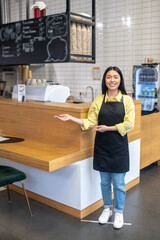 Fototapeta na wymiar Cute smiling waitress in a black apron standing near the cafe counter