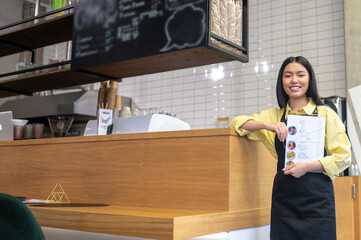 Cute smiling waitress in a black apron standing near the cafe counter