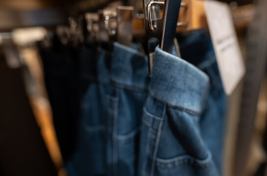 Blurred photo of denim pants in clothing store. Jeans on hanger hanging on rack in clothing store. Fashion retail shop inside shopping mall. Clothes on hangers in a clothes shop. Denim Jeans display.