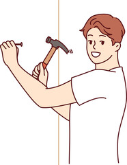 Man with hammer makes repairs in house by hammering nail into wall to hang picture
