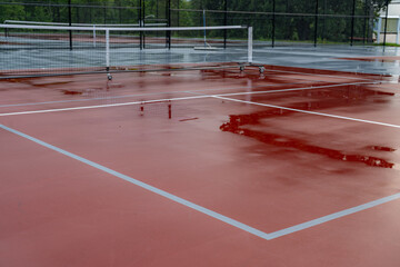 Wet red tennis court with white lines combined with gray pickleball lines