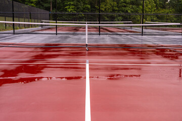 New portable pickleball nets on a wet red tennis court with white lines combined with gray...