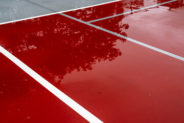 Wet red tennis court with white lines combined with gray pickleball lines