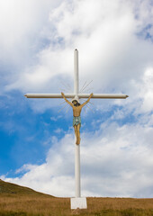 A close-up of a metal cross with Jesus crucified on a hillside against a sky background