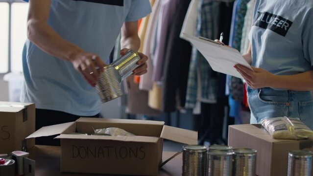 Male and female charity workers at food bank sorting through donations - shot in slow motion