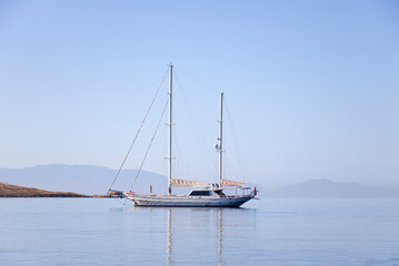 A single white sailing boat in blue aegean sea with mountain and sky in background, with copy space.