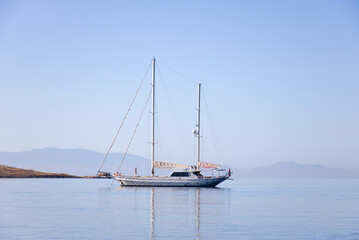 Fototapeta premium A single white sailing boat in blue aegean sea with mountain and sky in background, with copy space.