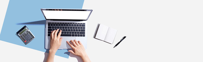 Person using a laptop computer with a notebook and a calculator