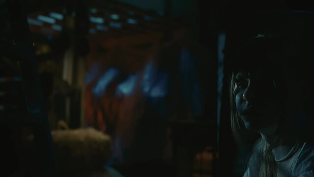 Blonde girl, victim of the horror maniac hiding from the man with a chainsaw behind the barrel.