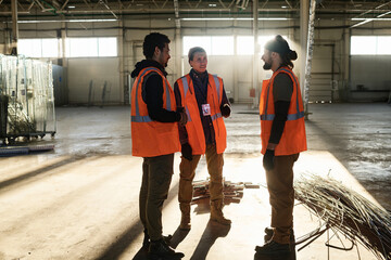 Group of three young intercultural builders in workwear discussing working points at meeting while...