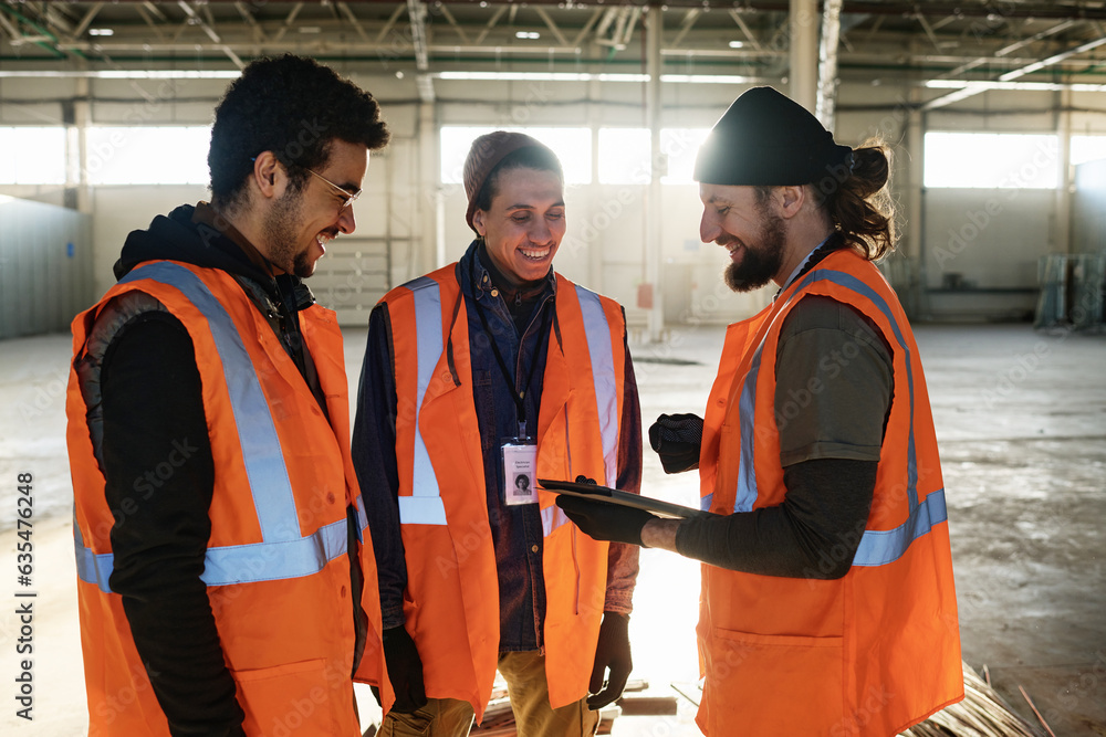 Poster three happy young male workers of warehouse discussing presentation points while one of them holding