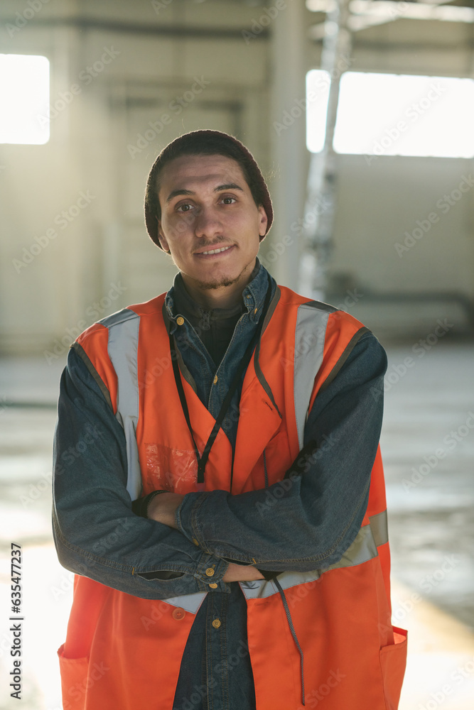 Poster happy young engineer or foreman in protective fluorescent vest looking at camera with his arms cross