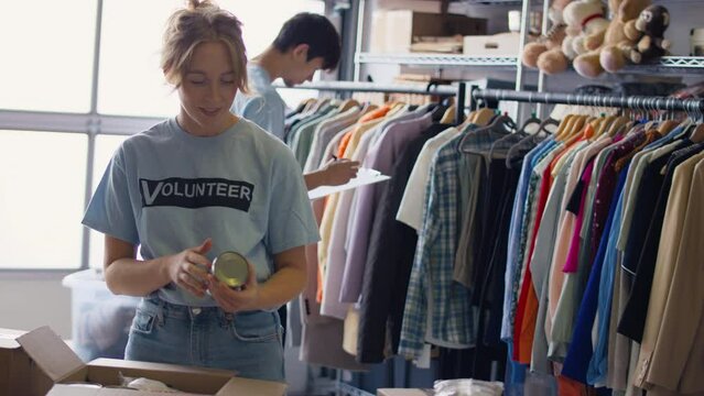 Male and female charity workers sorting through donations of food and clothing - shot in slow motion