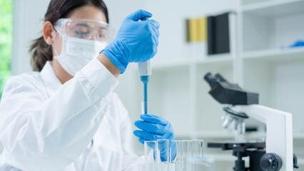 Asian woman scientist is dropping blue liquid substance in science test tube in laboratory. Concept of science, biochemistry, chemical, diagnosis, biotechnology. Substance study analyzing experiment