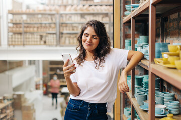 Happy ceramic store owner reading a text message in her shop