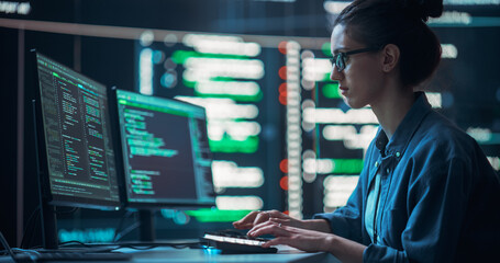 Medium Shot of a Woman Working as a Developer, Surrounded by Big Screens Displaying Lines of Code in a Monitoring Room. Female Programmer Using Desktop Computer, Analysing Data, Creating AI Software - obrazy, fototapety, plakaty
