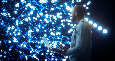 Portrait of Young Black Man Working on Laptop Computer, Looking at Big Digital Screen Displaying Neural Network Visualisation in 3D. Professional Data Specialist Analysing User Information Concept.