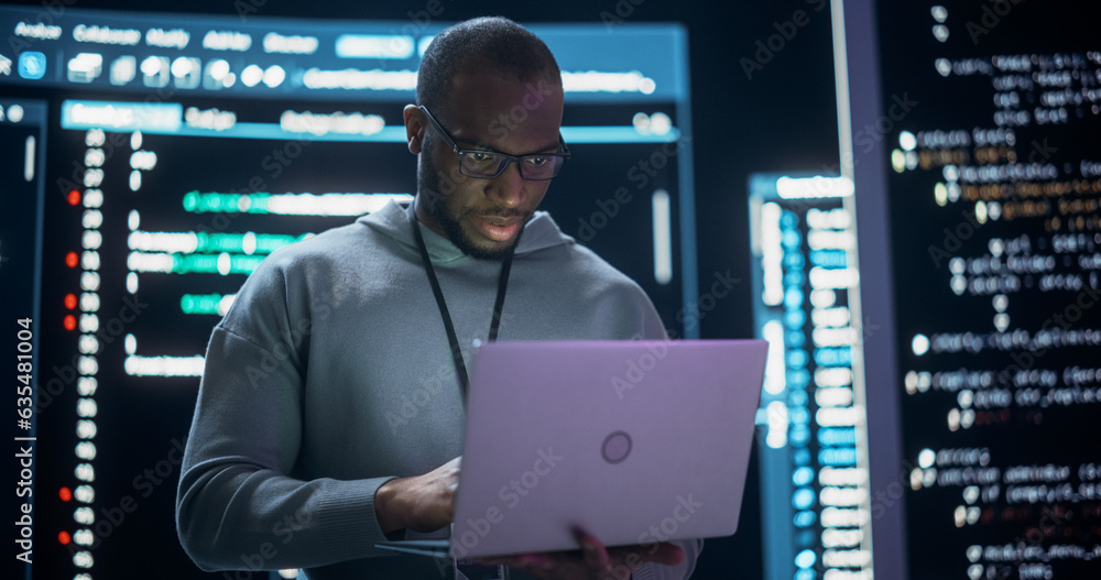 Poster Portrait of Professional Programmer Developing a Big Data Interface Software Project.Young Black Man Working on Laptop Computer, Looking at Big Digital Screen Displaying Back-end Code Lines