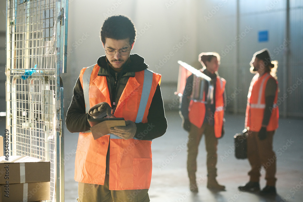 Leinwandbilder young serious engineer in workwear scrolling in tablet while standing in front of camera against col