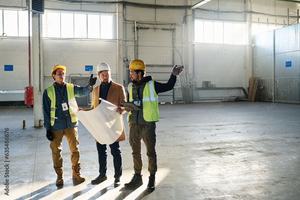 Poster two of three young engineers pointing aside while consulting or explaining something to serious cont