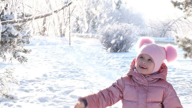 Child playing in the park on winter day having fun jumping and wallowing in the snow, shakes off snow from branches, winter active games  outdoors
