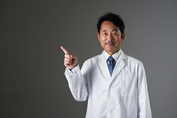 左側を指差すミドルエイジの医者　黒背景