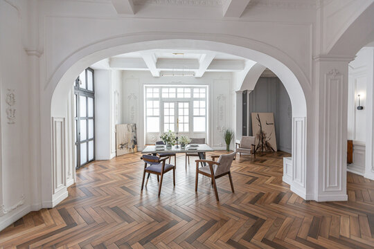 a chic expensive bright interior of a huge living room in a historic mansion with arched arches, columns and white walls decorated with ornaments and stucco.