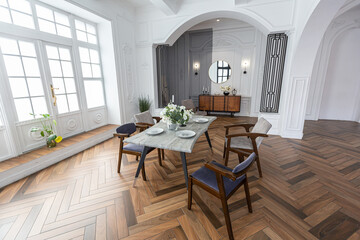 a view of a set dining table in a chic expensive bright interior of a huge living room in a historic mansion with arched arches, columns and white walls decorated with ornaments and stucco.