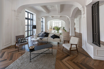 a chic expensive bright interior of a huge living room in a historic mansion with arched arches, columns and white walls decorated with ornaments and stucco.