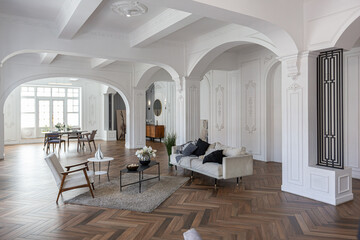 a chic expensive bright interior of a huge living room in a historic mansion with arched arches, columns and white walls decorated with ornaments and stucco.