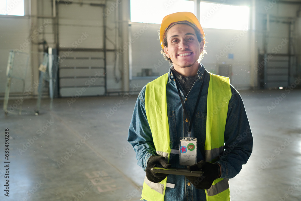Leinwandbilder young successful engineer or builder in protective workwear looking at camera with smile while stand