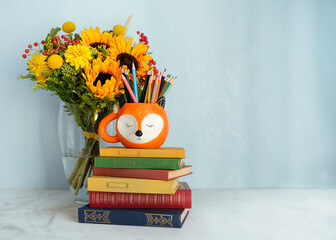 autumn flowers bouquet, pencils in fox shape cup and books on table. back to school concept. autumn...