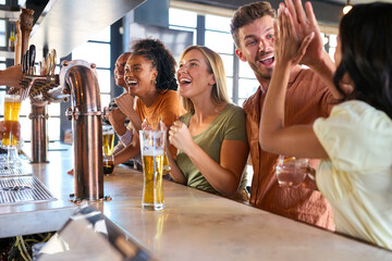 Multi-Cultural Group Of Friends In Sports Bar Celebrating As They Watch Game On TV
