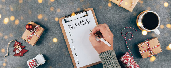 Woman's hand writing 2024 Goals in notebook. Top view, flat lay. Banner - 635494696