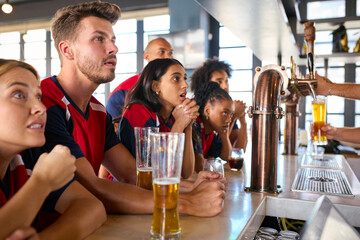 Multi-Cultural Group Of Friends Wearing Team Shirts In Sports Bar Celebrating Watching Game On TV