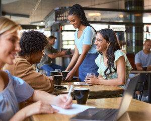 Woman Working On Laptop In Foreground With Couple Meeting Socially Behind In Busy Coffee Shop