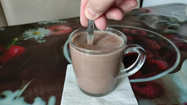 Man stirring with a spoon of cocoa in a transparent mug, 4K video