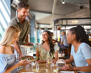 Group Of Female Friends Meeting Up In Restaurant Being Served Meal By Waiter