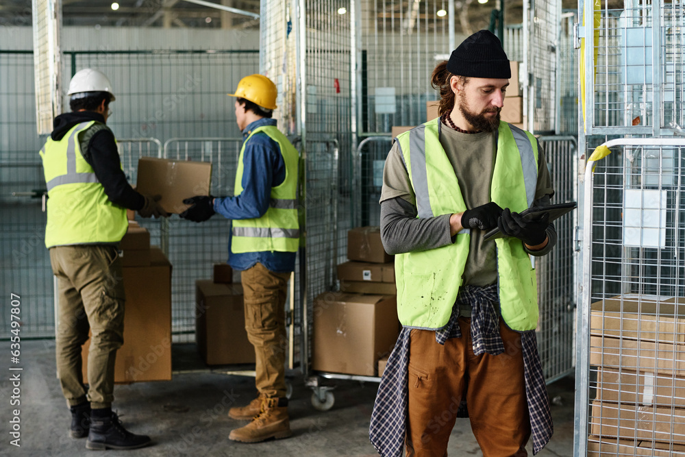 Leinwandbilder young serious male engineer in reflective jacket looking at tablet screen while networking or lookin