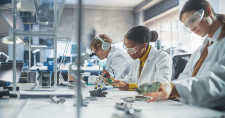 Team of Multiethnic Science Students Conducting Electronics Experiments in a University Workshop. Diverse Young Classmates Using Microscopes, Working with Soldering Iron to Create a Circuit Board