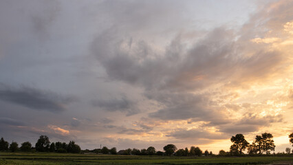 A cloudscape half gray half orange because of the bright light of sunset. There is rural land down below 