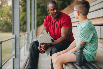 Sports coach talking to a young kid outside in a school