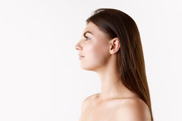 Side view image of young beautiful woman with brown straight hair, bare shoulders against white studio background. Concept of female beauty, skin care, cosmetology and cosmetics, health, ad