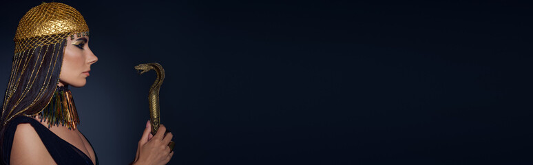 Side view of woman in egyptian headdress holding crook in snake shape on blue background, banner