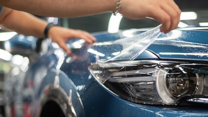The master in the car service applies a protective armor film to the car body.  - obrazy, fototapety, plakaty